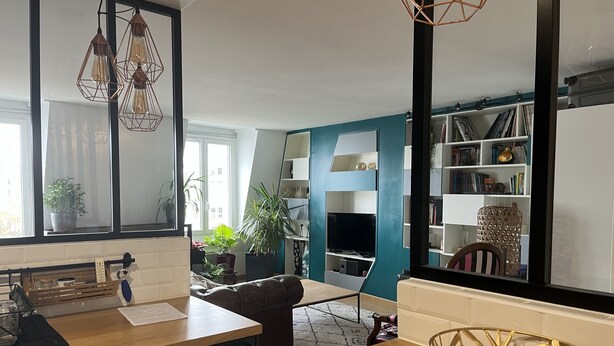Une cuisine moderne avec un plan de travail en bois, un coin repas avec une table et une bibliothèque remplie de livres et d’objets décoratifs.