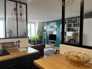 A modern kitchen with a wooden countertop, a dining area with a table, and a bookshelf filled with books and decorative items. - Beaubourg Saint-merri le Marais (Paris)