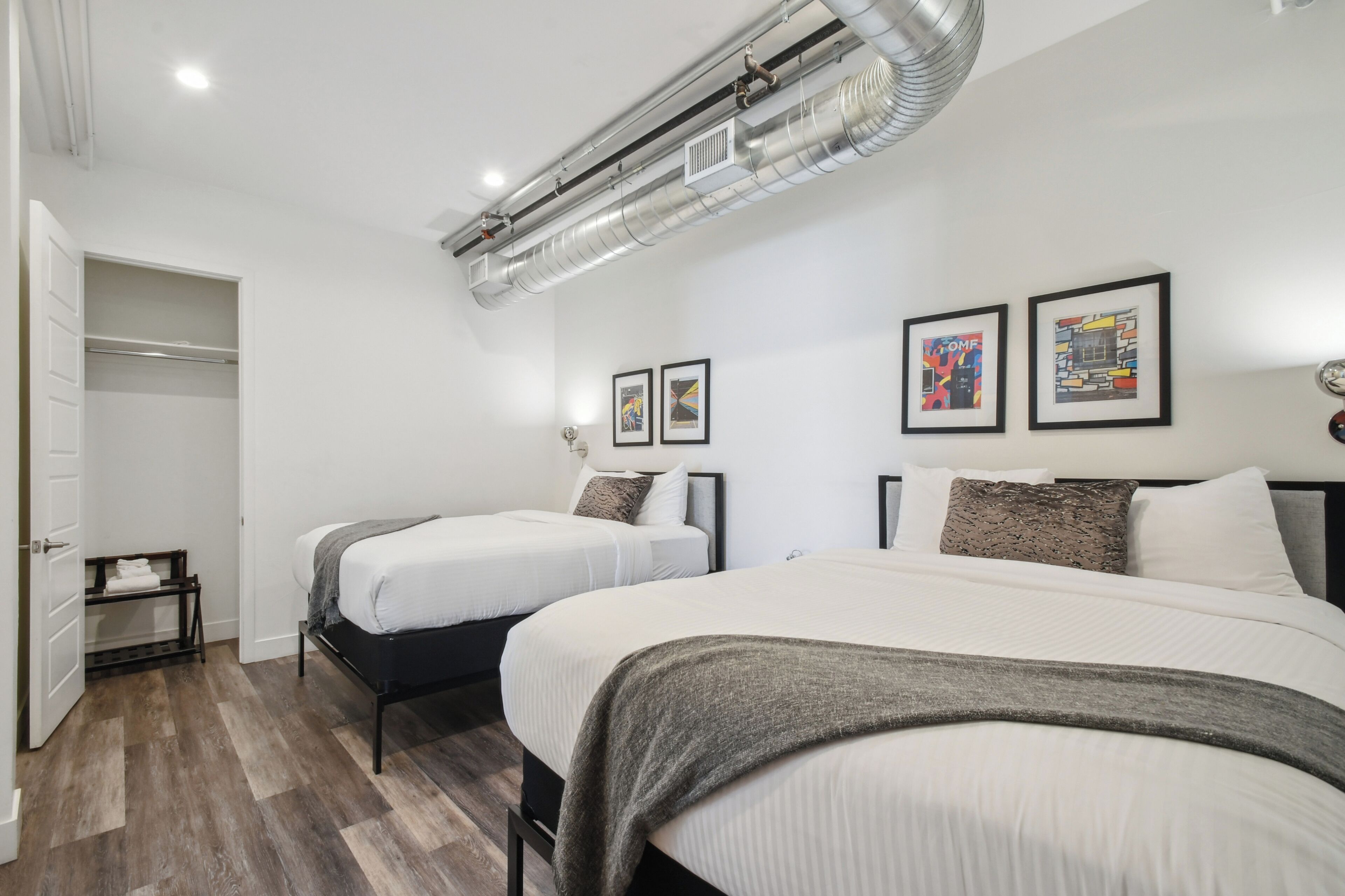 A modern hotel room with two beds, a walk-in closet, and artwork on the walls.