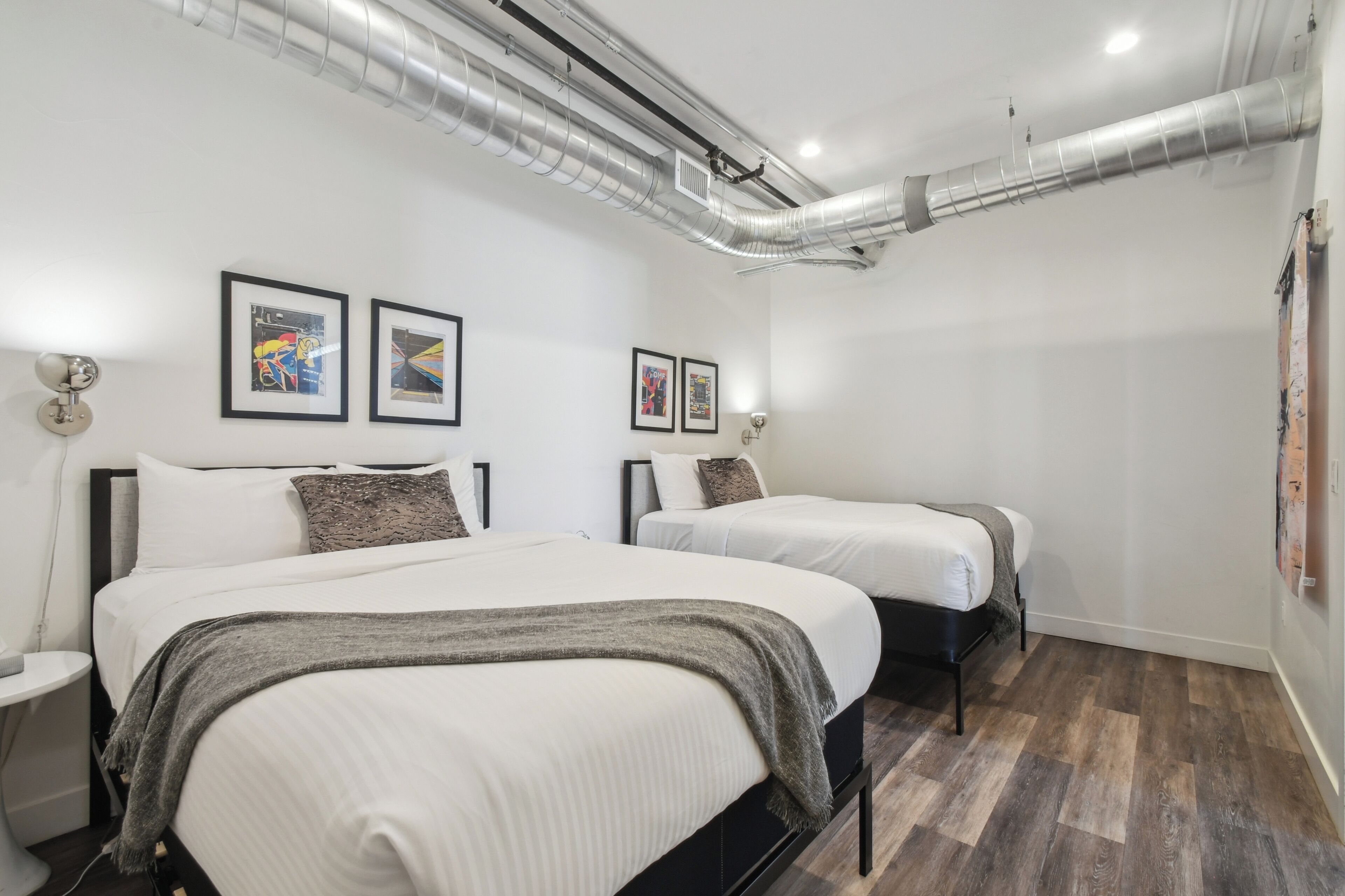 A modern hotel room with two beds, a white color scheme, and artwork on the walls.