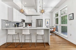 A modern kitchen with a white island, bar stools, and a large window. - Dog-Friendly 2BR Boho Loft in RiNo | Walk to Mission Ballroom & Breweries (Denver)