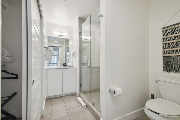 Une salle de bain moderne avec une douche à l’italienne en verre, des toilettes et un lavabo blanc avec un miroir au-dessus.