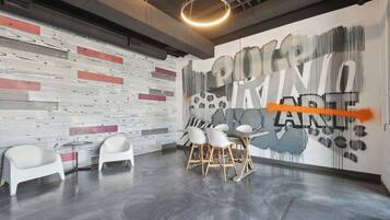 Una sala de conferencias moderna con diseño de pared de madera y metal, una mesa redonda con sillas y un gran mural abstracto.