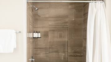 Une douche avec une porte en verre, un porte-serviettes avec une serviette blanche et trois bouteilles sur une étagère.
