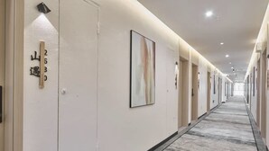 A hotel corridor with numbered doors, a framed abstract painting, and a patterned carpet. - QianYue Hotel (Wuzhou)