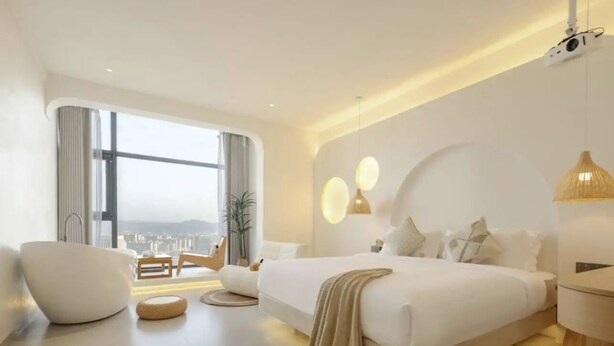 A modern bedroom with a large bed, a seating area, and a view of the city. - QianYue Hotel (Wuzhou)