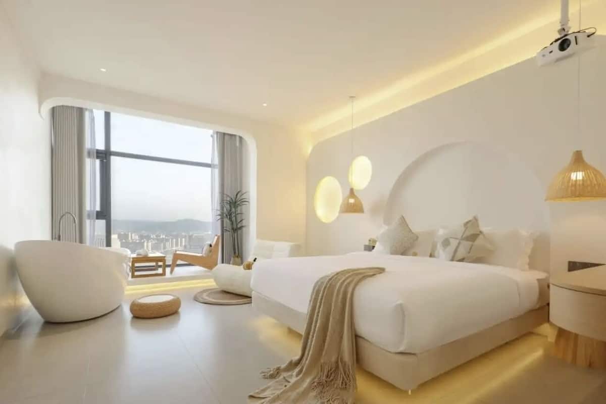 Un dormitorio moderno con una cama grande, un rincón de descanso y vistas a la ciudad.