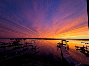 Un atardecer sobre un lago tranquilo con muelles de madera y una zona de estar cubierta.