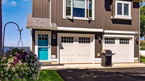 Une maison à deux étages avec un garage, une porte bleue et un parterre de fleurs dans le jardin.