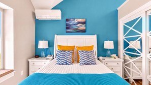 A bedroom with a bed, two bedside tables, a nightstand, a wall-mounted air conditioner, and a window.