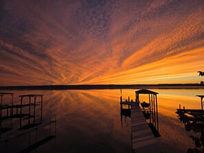 Un atardecer sereno sobre un lago tranquilo con muelles de madera y una zona de estar cubierta.