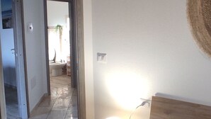 Et soveværelse med en seng, et natbord og en lampe. En dør fører til et andet rum.
