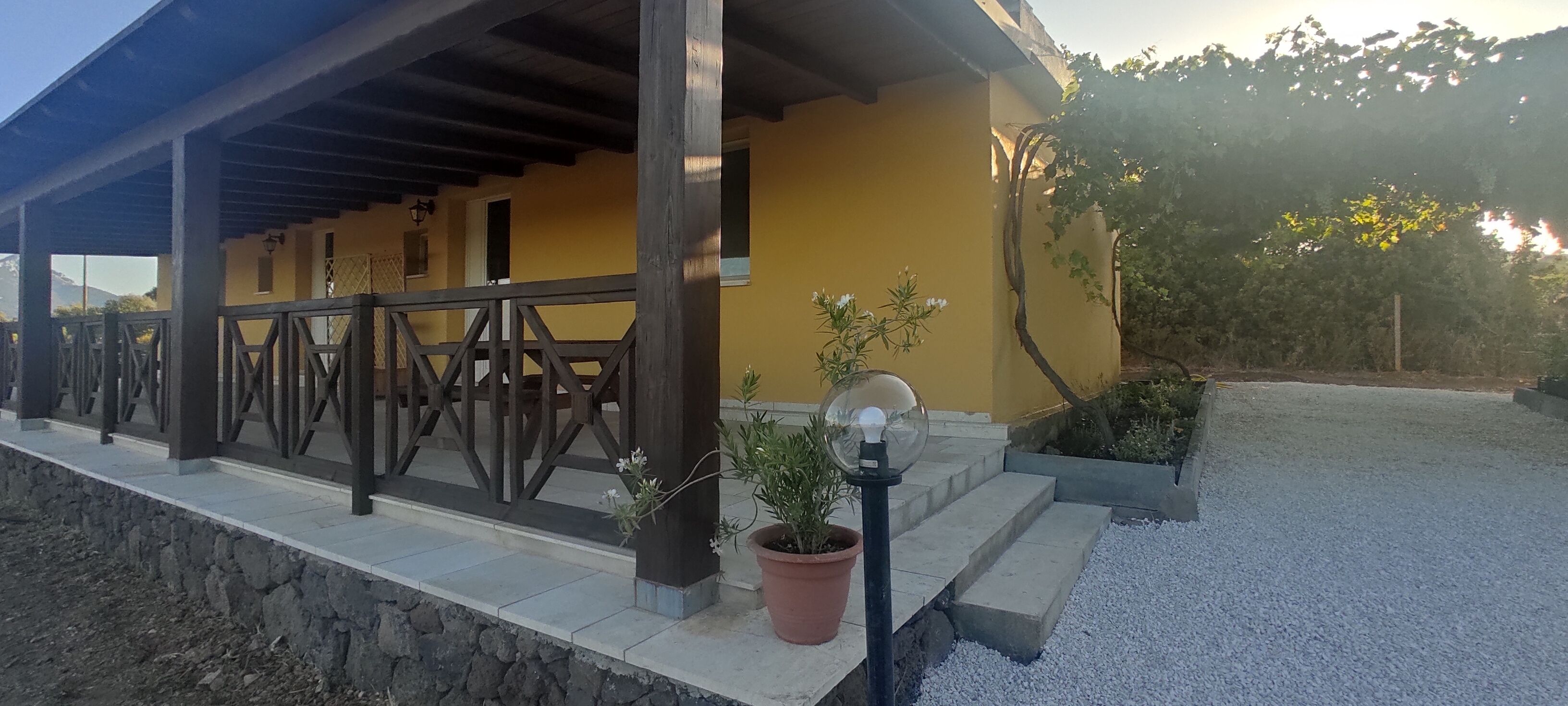 A covered outdoor area with a stone wall, wooden railing, and potted plants.
