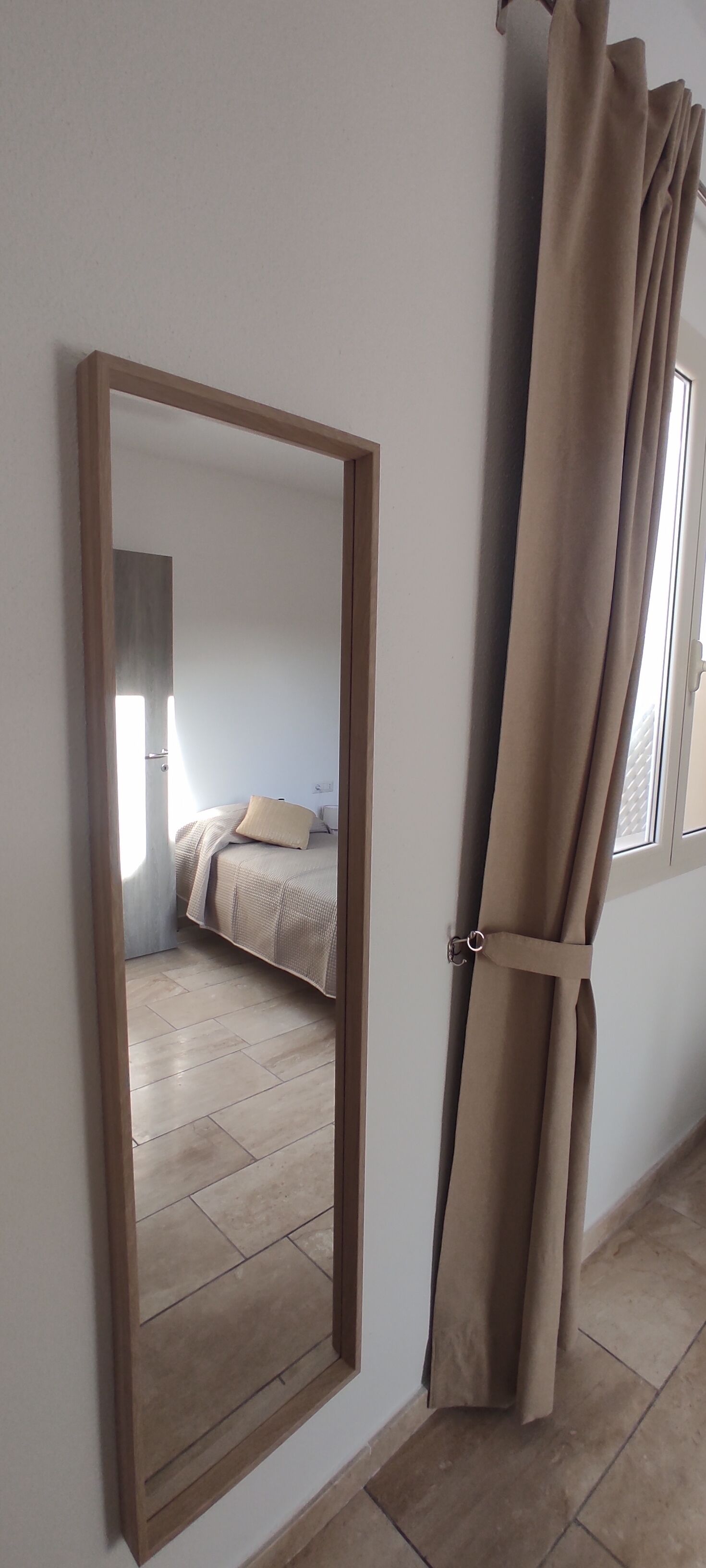 A bedroom with a bed, a mirror, and a curtain.