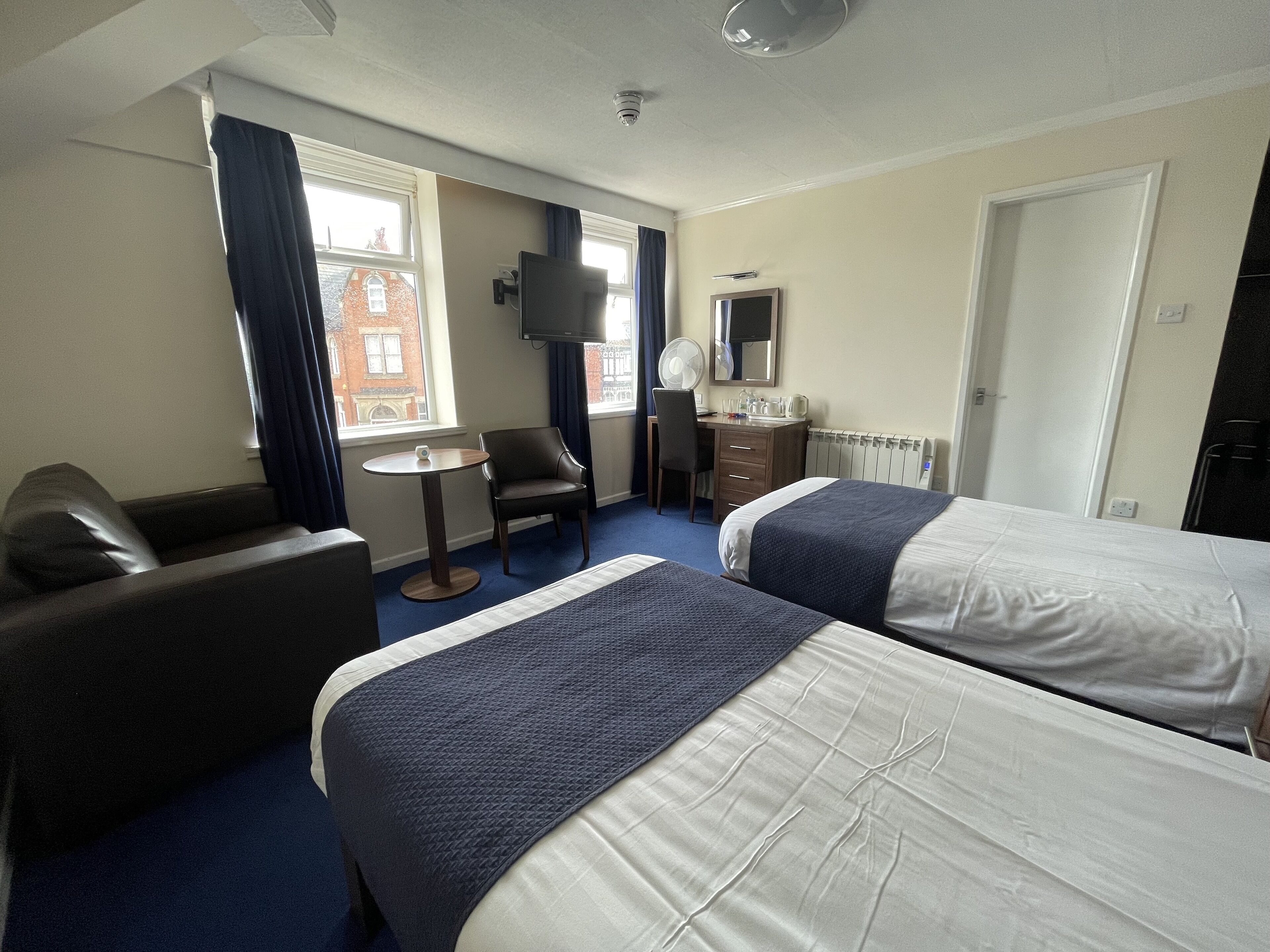 A hotel room with two beds, a desk, a chair, a TV, and a window with curtains.