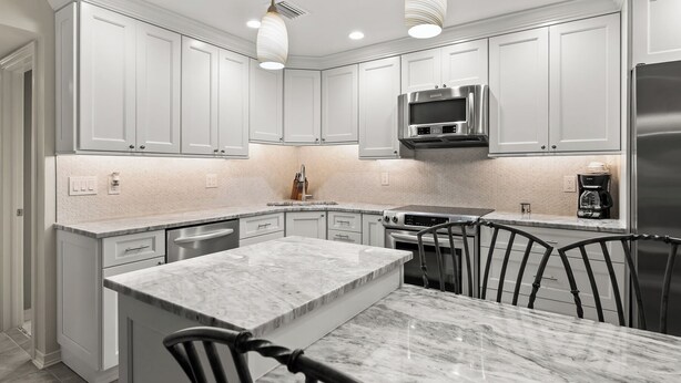 Une cuisine moderne avec des meubles blancs, un îlot central, des appareils en acier inoxydable et des luminaires suspendus.