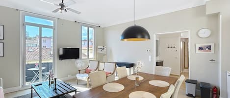 A spacious dining area with a wooden table and chairs, a ceiling fan, and a large window providing a view of the city.