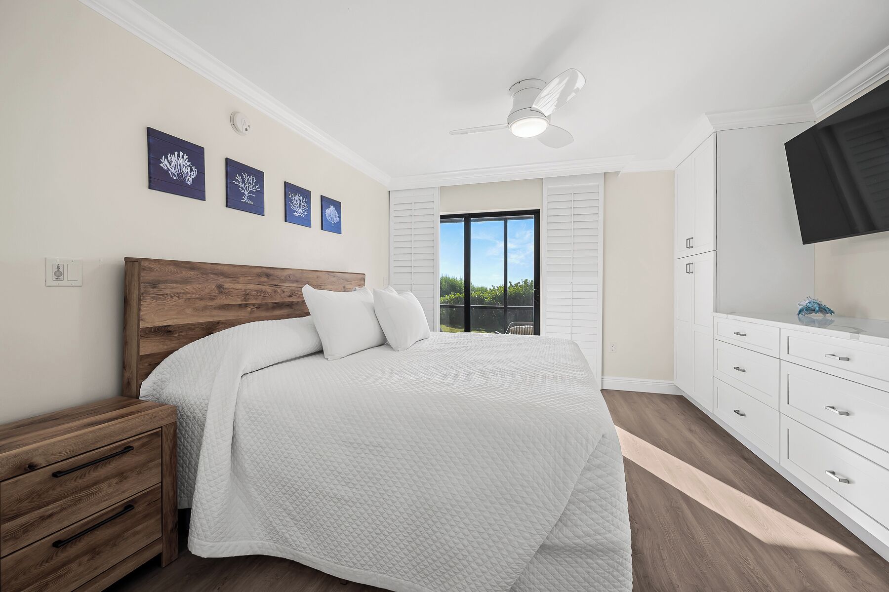Une chambre à coucher avec un lit, une table de chevet en bois, une commode blanche et un ventilateur de plafond.