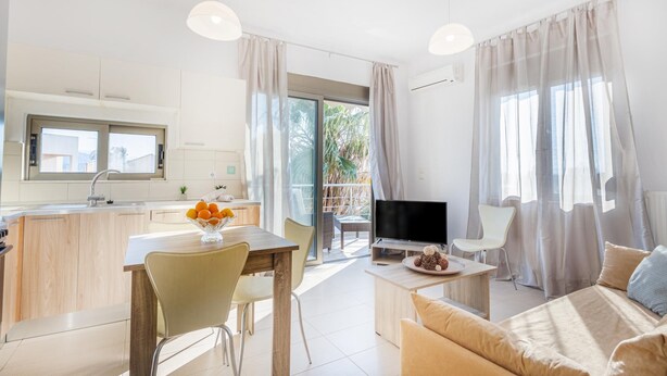 Un soggiorno moderno con un divano, un tavolo da pranzo con sedie, una TV e un balcone con tende.