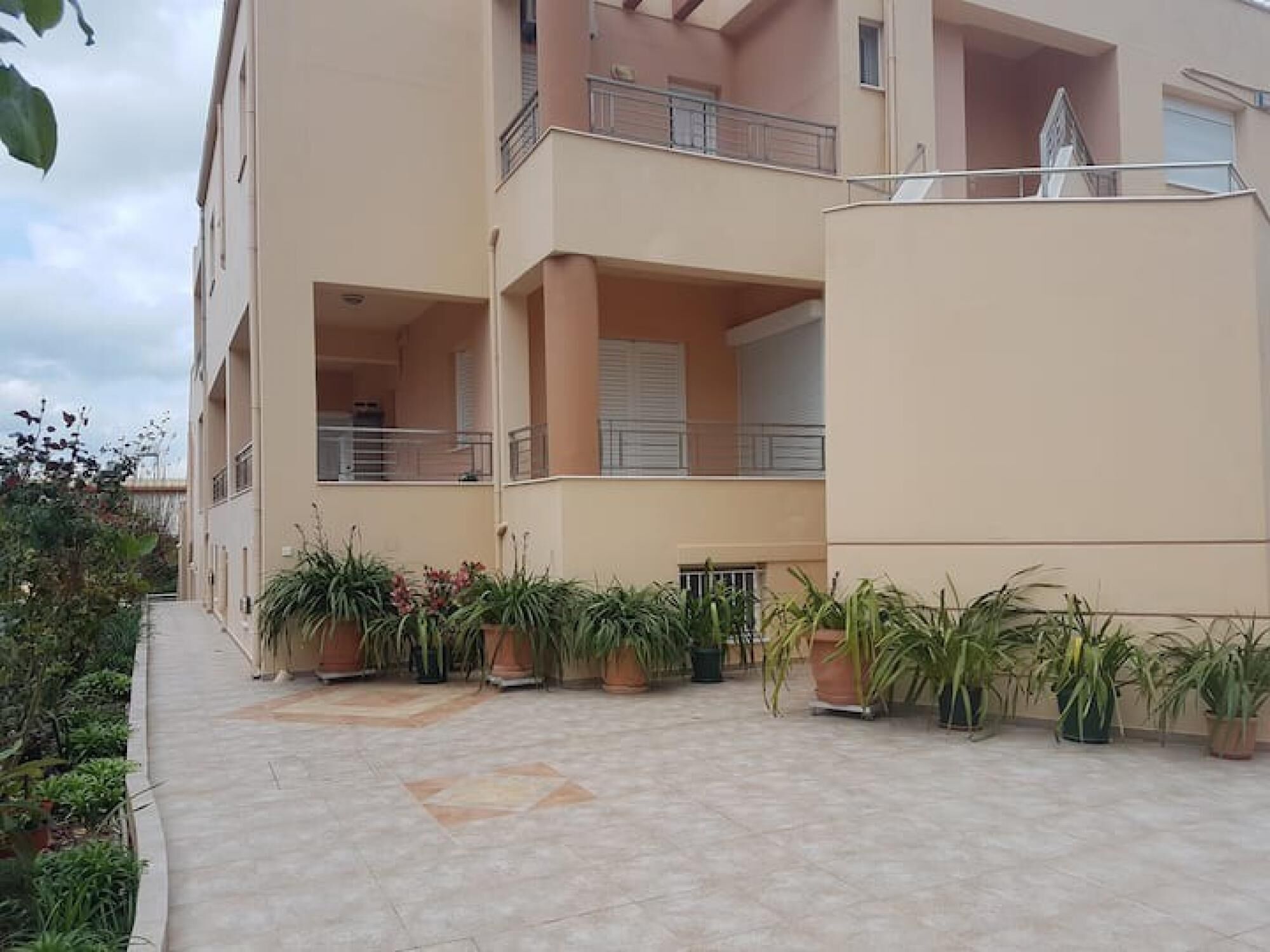 A multi-story residential building with balconies, potted plants, and a tiled walkway.