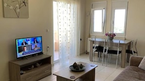 Ett vardagsrum med en TV, trämöbler, en matplats och ett fönster med gardiner.