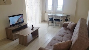 Ett vardagsrum med en TV, en soffa, ett soffbord och en matplats med stolar och ett bord.