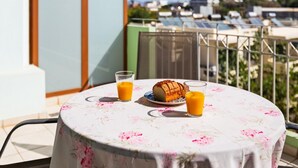 A round table with a floral tablecloth, a loaf of bread, and two glasses of orange juice on a balcony with a city view. - Emmanouel Maisonette Near the Sea (Chania)