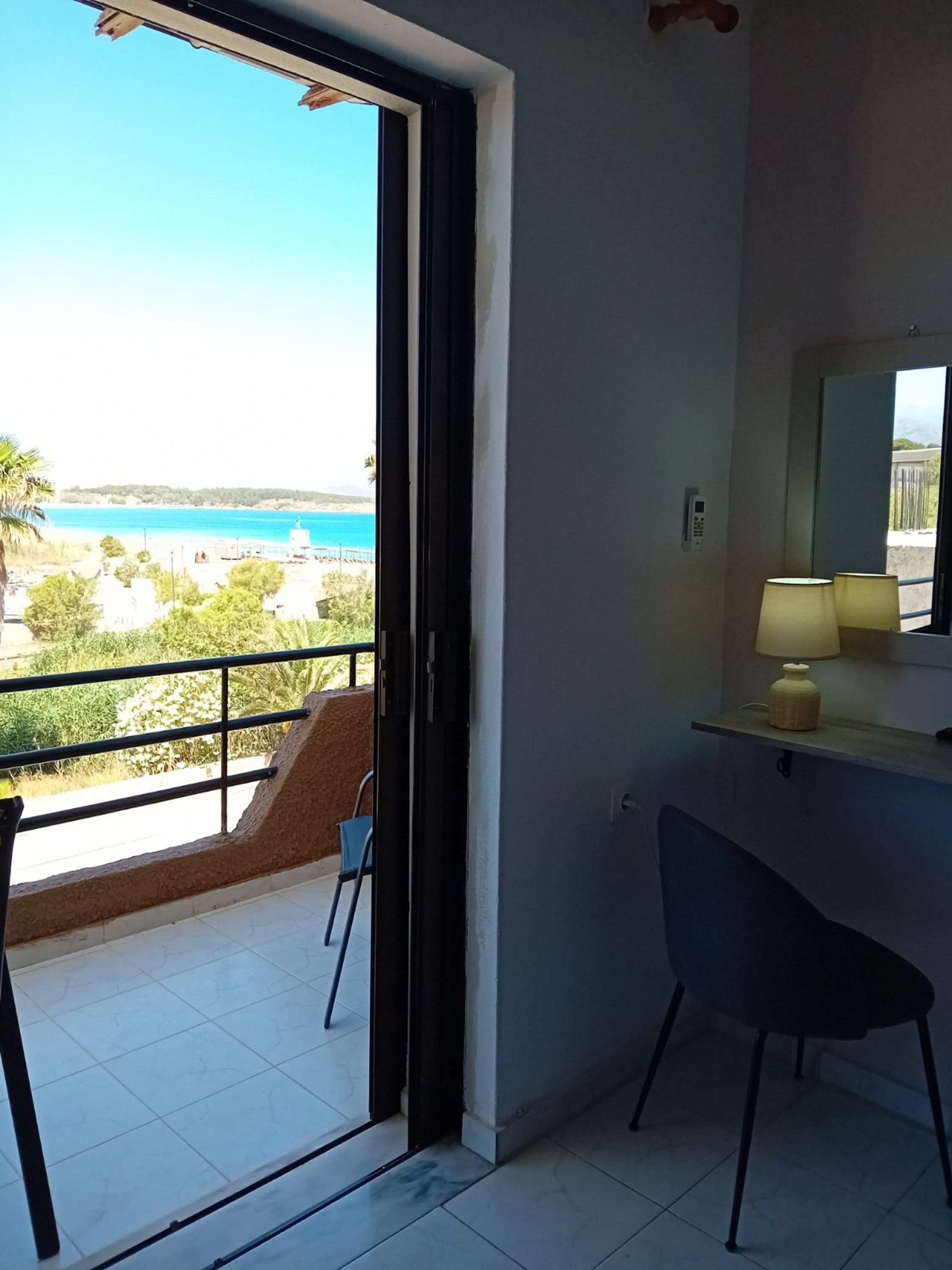 A room with a balcony, a chair, a lamp, and a view of the sea.