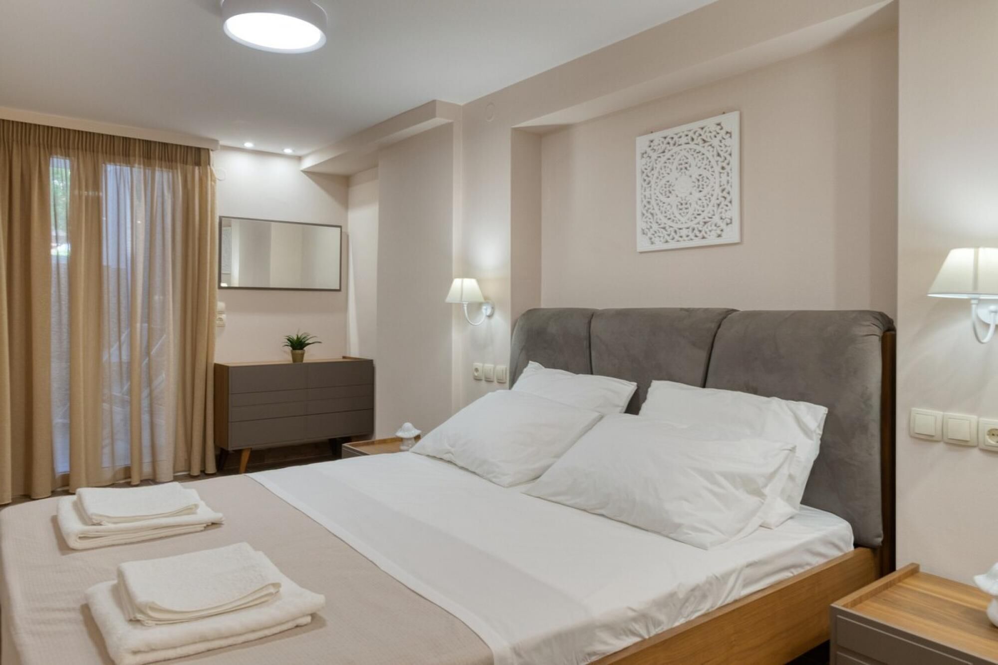 Un lit bien fait, avec du linge de lit blanc, une table de chevet avec une lampe, une commode et un élément décoratif mural.