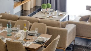 Un espace repas moderne avec des canapés en cuir, une table en bois dressée pour le repas et un téléviseur posé sur une étagère en bois.
