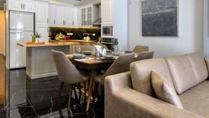 Une cuisine moderne avec des meubles blancs, un pare-feu en marbre et un coin repas comprenant un canapé et des chaises de couleur beige.