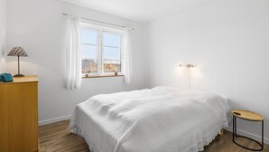Un dormitorio con cama, escritorio, lámpara y ventana con cortinas.