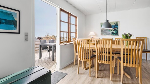 Un comedor con mesa y sillas de madera, una lámpara colgante y vistas a través de un ventanal.