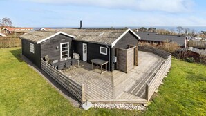 Una casa de madera de dos pisos con un balcón, una pequeña cocina al aire libre y vista al mar.