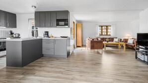 Una cocina moderna con armarios grises, una isla central y una zona de comedor con sofá marrón y mesa de madera.