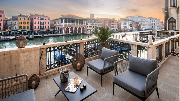 Eine Terrasse mit Sitzgelegenheiten, Blick auf einen Kanal und historische Gebäude im Hintergrund.