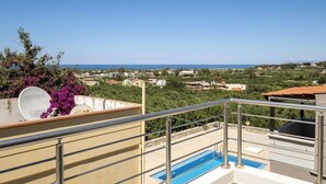 A balcony with a pool, overlooking a coastal landscape with houses and greenery. - Kayzo Luxury Apartment With Pool (Platanias)