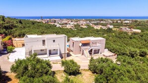 A residential area with modern houses, a clear view of the sea, and a lush green landscape. - Kayzo Luxury Apartment With Pool (Platanias)