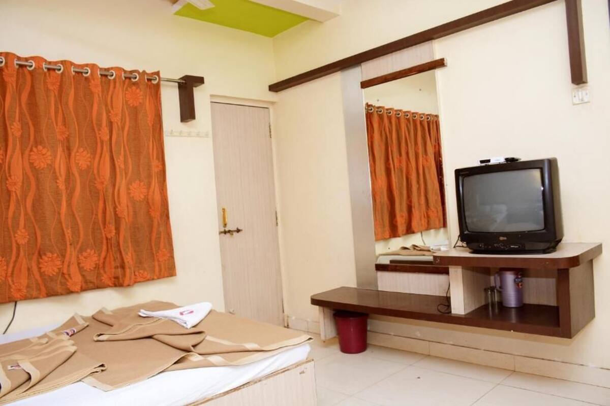 A bedroom with a bed, a television on a wooden stand, a mirror, and orange curtains.