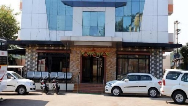 Un edificio de varios pisos con una fachada destacada en amarillo y azul, un letrero que dice "Varsha" y un estacionamiento con varios autos y motocicletas.