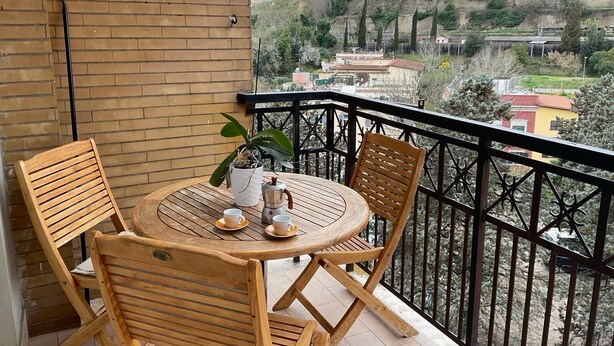 A wooden table and chairs on a balcony with a view of a hilly landscape. - Valle Aurelia vatican apartment: Your Charming Retreat bear S.Peter (Roma)
