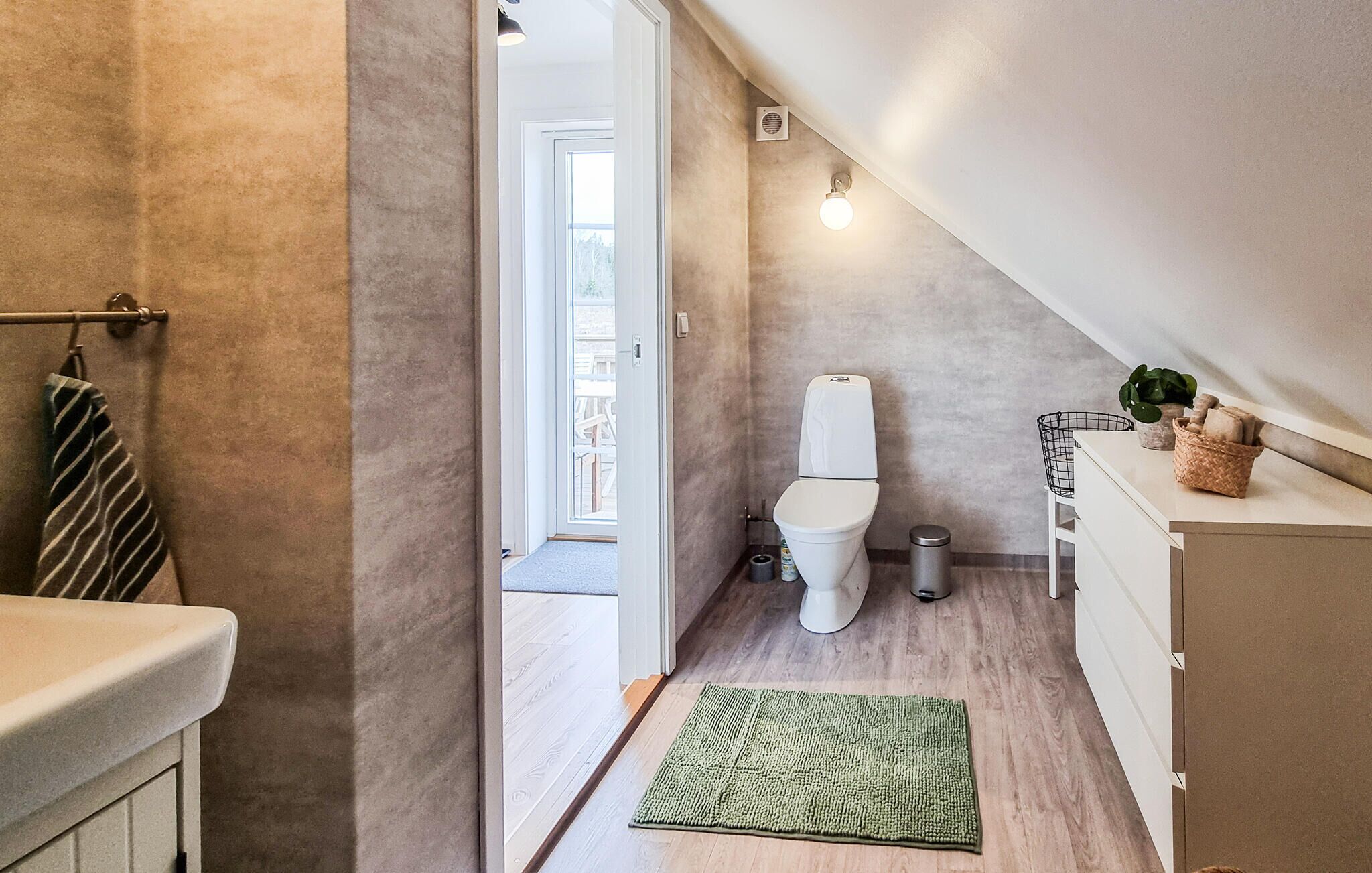 Een moderne badkamer met toilet, een klein prullenbakje, een groene mat en een handdoekhouder.