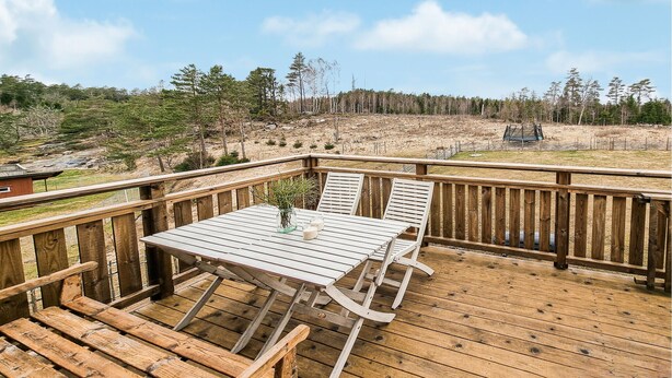A wooden deck with a table and chairs, overlooking a forested area.