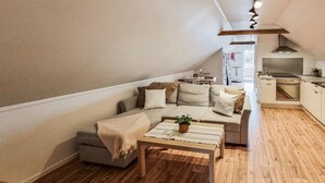 A cozy living room with a sectional sofa, a coffee table with a plant, and a kitchen area with wooden flooring and white cabinets.