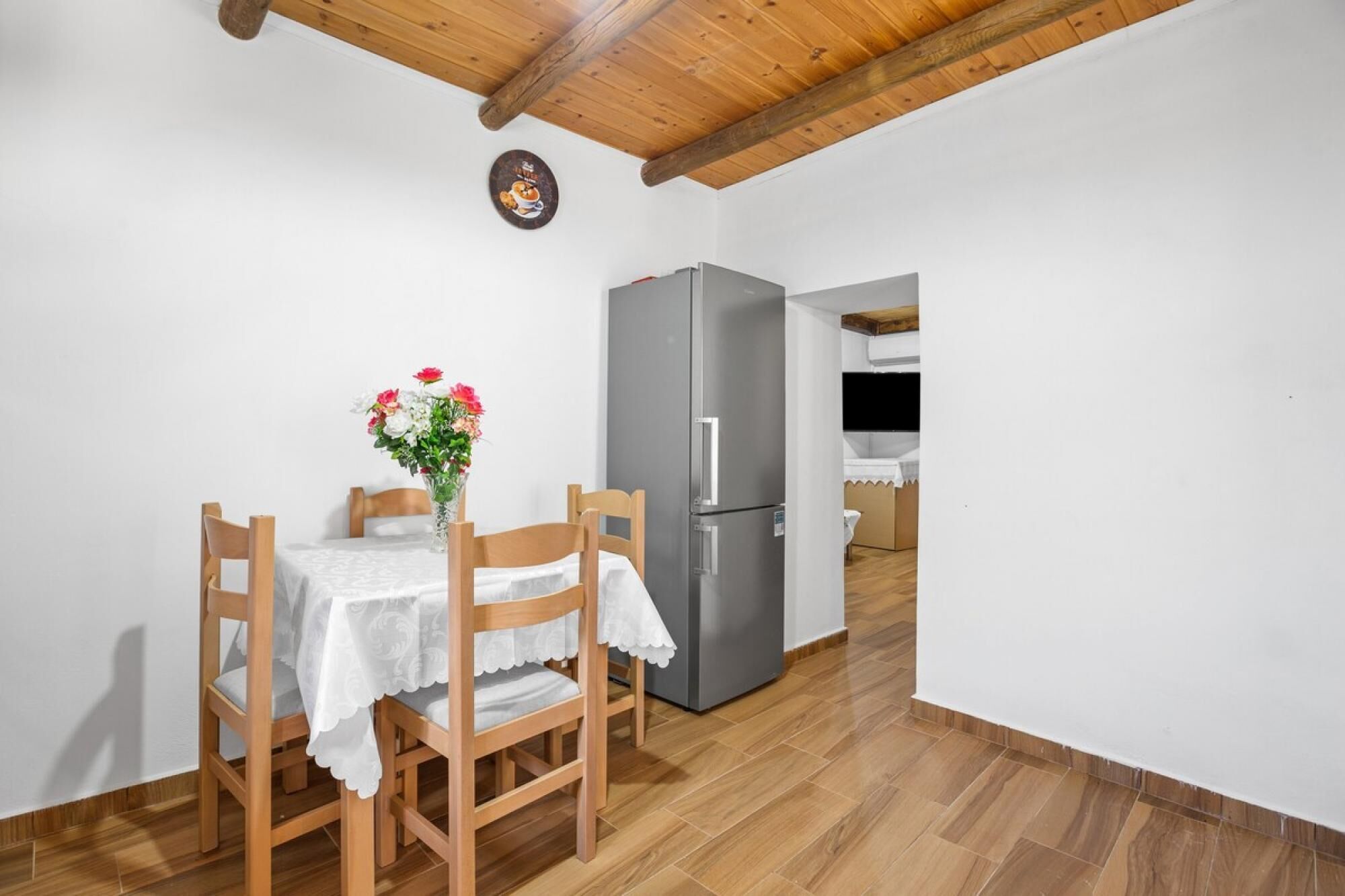 Un petit coin repas avec une table et des chaises en bois, un réfrigérateur et un vase à fleurs.