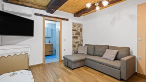 A cozy living room with a wooden floor, a grey sectional sofa, a flat-screen TV, and a stone accent wall. - Maria s House With View in Kambos (Kissamos)