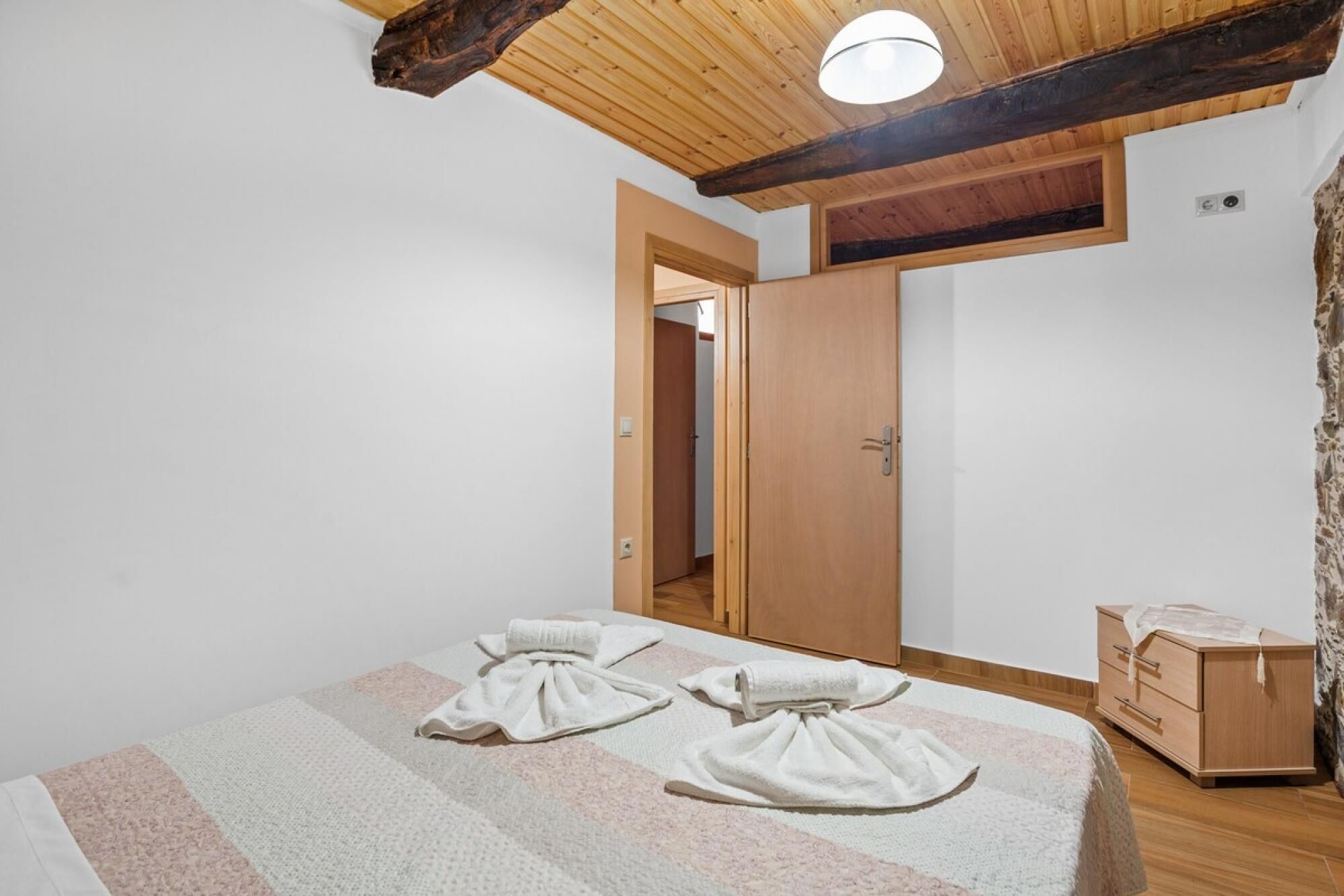 Ein Schlafzimmer mit einem Bett, zwei Handtüchern, einer Holzkommode und einer Tür zu einem anderen Raum.