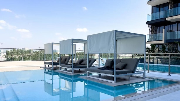 A rooftop pool area with lounge chairs and a glass balustrade. - Luxe 1BR 15Mins- Beach Best Infinity Pool -Jumeirah Village Circle ,JVC  (Dubai)