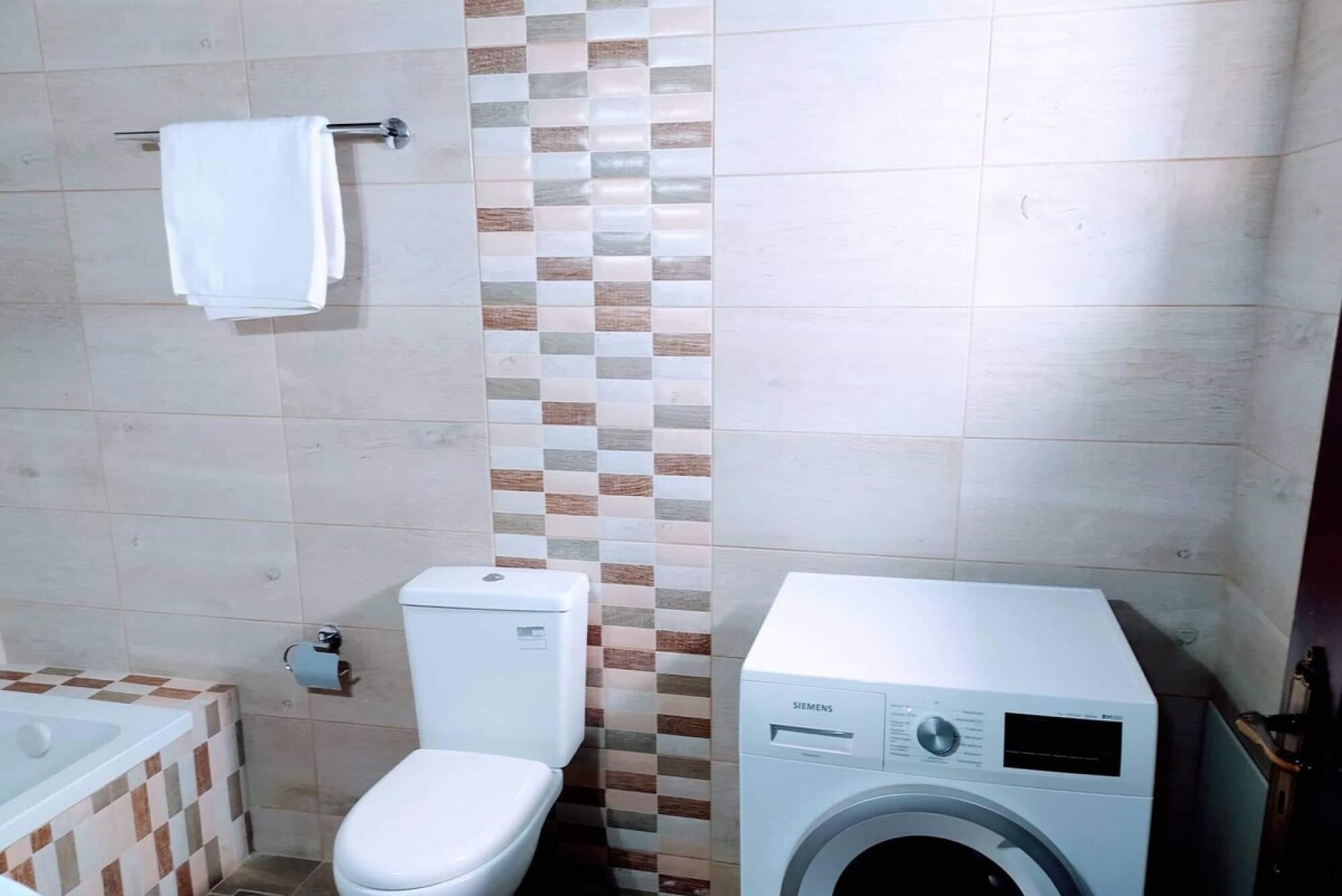 Casa de banho com sanita, máquina de lavar roupa e banheira.
