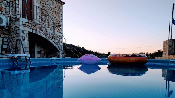 A swimming pool with two inflatable rings, a stone building, and a clear sky. - Traditional Villa in Pemonia (Apokoronas)